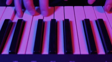 Müzisyenlerin elleri elektronik bir sentezleyicide melodi çalar. Yakın çekim, canlı pembe ve mavi neon ışıklarıyla aydınlanır ve karamsar bir atmosfer yaratır..