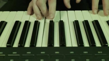 Erkek eller bir sentezleyici klavyesinde melodi çalar. Dinamik mor, mavi ve yeşil kulüp ışıkları sahneyi aydınlatıyor.