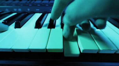 Müzisyenlerin elleri bir sentezleyici klavyesinde melodi çalar. Yakın çekim dinamik, renkli ışık kırmızı ve yeşilden maviye ve mora kayıyor..