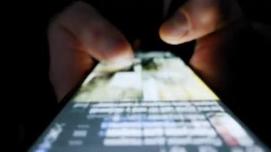 Eller akıllı bir telefondan sonsuz bir sosyal medyada geziniyor. Ekran, parmakları tamamen karanlık bir odada aydınlatıyor..