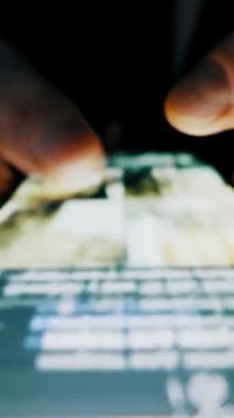 Akıllı telefon ekranındaki sosyal medya yayınında parmaklarını hızla kaydırıyor. Karanlık bir odada çekilen, sığ bir alan derinliği olan aşırı yakın çekim..