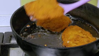 Kişi, sıcak dökme demir bir tavadan spatulayla altın kahverengi pirzola çıkarır. Yağlı baloncuklar ve çıtır çıtır etin etrafındaki cızırtılar iştah açıcı bir doku oluşturuyor..