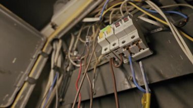 Eski elektrik kontrol panelinde üç devre kesici ve kaotik kablolar var. Tozlu metal kutunun içinde tehlikeli bağlantılar ve karmaşık kablolar var..