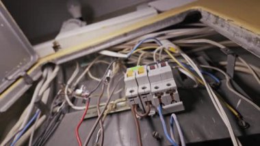 Radyasyona maruz kalan elektrik kabloları tozlu bir metal dağıtım kutusunun içindeki devre kesicilerin etrafına dolanır. Kamera kaotik kabloları ve potansiyel güvenlik tehlikelerini göstermek için geri çekiliyor.