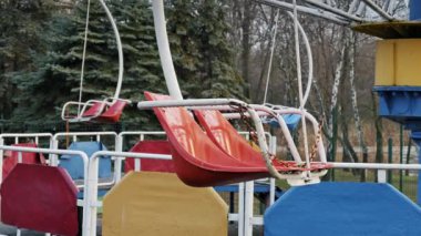 Terk edilmiş bir parkta sallanan eski bir salıncağın boş kırmızı koltukları. Bulutlu bir gün ve yıpranmış boya Sovyet sonrası melankolik bir atmosfer yaratır..