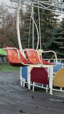 Eski, boş bir atlıkarıncadaki boş kırmızı salıncak ıssız bir parkta hareketsiz duruyor. Ahşap güverte ıslak ve düşmüş yapraklarla kaplı, melankolik ve yalnız bir atmosferi çağrıştırıyor..