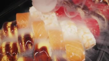 Somon, yılan balığı ve tobiko dürümleri de dahil olmak üzere çeşitli suşi türleri siyah bir tabakta otururlar. Taze deniz ürünleri aperatiflerinin üzerinde kalın beyaz buzlu sis akıyor..