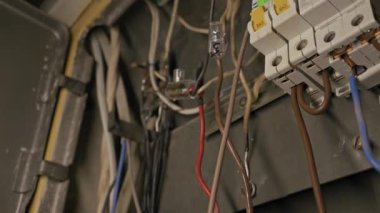 Electrical wires and circuit breakers connect inside a metal distribution box. Camera pans across chaotic cabling and fuse switches in dim lighting.