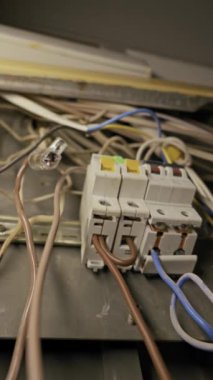 Açığa çıkan devre kesiciler tozlu metal bir elektrik kutusunun içindeki karmaşık kahverengi ve mavi kablolara bağlanıyor. Kamera, bakım gerektiren kaotik kablolar ve gevşek bağlantıları ortaya çıkarıyor..