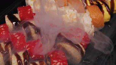 Çeşitli Japon suşileri somon ve tobiko ile birlikte siyah tepside dinleniyor. Ağır beyaz buz dumanı taze deniz ürünleri aperatiflerinin üzerine dağılır..