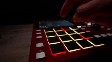 Parlayan kırmızı davul makinesi örneklerine dokunan beatmaker parmakları yakın plan. Müzik üretimi kavramı, elektronik yaratıcılık ve gece stüdyoları.