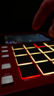 Bir müzisyen, karanlık bir stüdyoda yanan kırmızı bir davul makinesinin ritmik ritmine el vurur. Müzik üretimi, yaratıcı iş akışı ve modern elektronik sanatçılık kavramı.