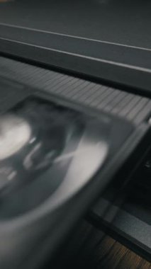 Elle siyah VHS kaseti eski tip video kaydedici sistemine yerleştirir. Mekanik yükleme mekanizması, tahta yüzeydeki koyu plastik kaplamanın içinde bant kabul ediyor.