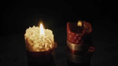 Bir el, karanlıkta sıcak bir parıltı yaratan iki balmumu mumunu kibritle yakar. Romantizm kavramı, bayram kutlaması, maneviyat ve rahat ev atmosferi..