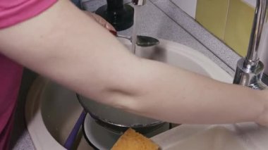 Kırmızı ojeli tanınmayan bir kadın gümüş bir kâse ve kaşığı musluk suyu akan bir lavaboda süngerle yıkıyor. Günlük ev işleri, ev işleri ve temizlik kavramı.