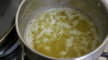 Sarı eritilmiş tereyağını kapayın ve gaz ocağında gümüş bir tencerenin içinde kaynayın. Mutfak hazırlığı, pişirme malzemeleri ve tereyağı yapma kavramı..