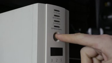 Bir erkek parmak, beyaz UPS yedek batarya ünitesindeki dairesel güç düğmesine basarak LED durum ışıklarını aktifleştiriyor. Elektrik güvenliği, gerilim koruması ve veri güvenliği kavramı.