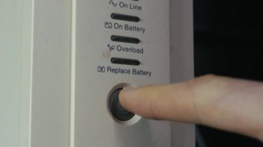 Kehribar ışığını aydınlatmak için beyaz bir UPS cihazının güç düğmesine basan bir parmağın yakın çekimi. Enerji güvenliği kavramı, yedek güç çözümleri ve elektrik güvenliği.