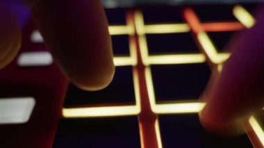 Müzisyen parmaklarıyla bir MIDI kontrolörünün ışıklı pedlerini tıklatıyorlar. Elektronik müzik üretimi, ses tasarımı ve gece hayatı kavramı.