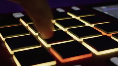 Profesyonel bir örnekleyicinin arka ışıklandırma pedlerine ritmik bir şekilde dokunan bir müzisyenin yakın çekimi. Elektronik müzik üretimi, yaratıcılık ve modern ses teknolojisi kavramı.