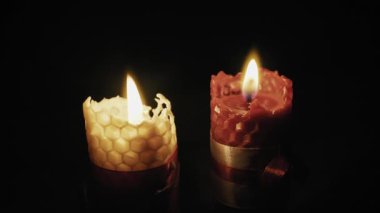 İki bal peteği bal mumu mumu, biri sarı ve biri kırmızı, zifiri karanlık bir zemin üzerinde parlak bir şekilde yanar. Romantizm kavramı, manevi meditasyon, tatil sıcaklığı ve rahatlama..