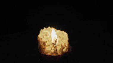 Karanlığa karşı titreyen bal peteği desenli yanan sarı balmumu mumuna yakın plan. Maneviyat, rahatlama, umut ve dini atmosfer kavramı.
