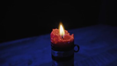 Kıvrımlı kırmızı sütun mumu parlak bir şekilde yanıp sönen sarı alevle koyu mavi bir arkaplanda yanar. Maneviyat, umut, anma ve karanlıkta sessiz meditasyon kavramı..