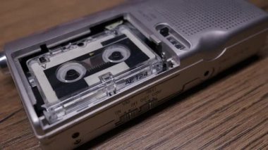 Gümüş bir mikrokaset kaydedici, operasyon sırasında sürekli dönen kasetleriyle ahşap bir masanın üzerinde oturur. Araştırmacı gazetecilik kavramı, klasik teknoloji ve geçmişe dönük gözetim..