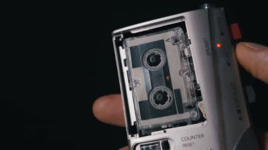 Bir başparmak gümüş bir mikrokasetçalar üzerindeki kırmızı kayıt tuşuna basarak kasetin dönmesini sağlar. Retro gazetecilik kavramı, analog teknoloji, izleme ve anıların korunması..