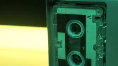 Gümüş mikrokaset kaydedici, değişen neon renklerin arka planına karşı dönen makaralarla çalışır. Retro teknoloji, casusluk, 80 'lerin nostaljisi ve analog ses izleme kavramı..