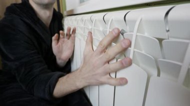 Close up of male hands feeling white wall heater surface to assess thermal output. Concept involves managing rising energy costs and household utilities during freezing winter.