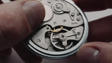 Kapalı bir makro görünüm, elle tutulan gümüş kaliteli bir cep saatinin karmaşık iç dişlilerini gösterir. Zaman geçirme kavramı, hassas mühendislik ve tarihin detaylı mekaniği..