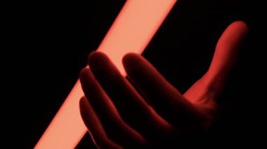 Bir el karanlıkta parlayan kırmızı neon tüpü kavrayıp dokunur. Bu konsept gelecekteki enerji, gizem ve dramatik ışıklandırma etkilerini taşır..