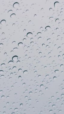 Camdaki yağmur damlacıkları yumuşak bulutlu bir gökyüzüne karşı. Bu dikey görünüm mobil için idealdir. Hava, melankoli ve sükunet kavramı.
