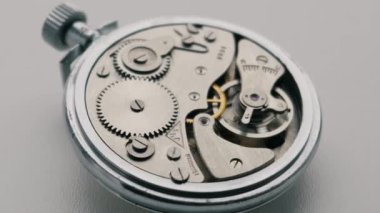 Gümüş bir cep saatinin iç mekanizması karmaşık pirinç dişlileri ve çelik yayları ortaya çıkarmak için döner. Zaman yönetimi, hassas mühendislik ve tarihsel zanaat kavramı.