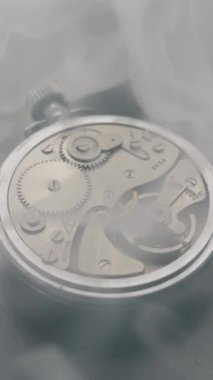 Eski model mekanik kronometrenin, dişliler ve hareket eden bir denge çarkıyla detaylı görüntüsü. Duman, metal bileşenlerin üzerinde yavaşça sürükleniyor. Kavram, geçen zamanı gösterir.