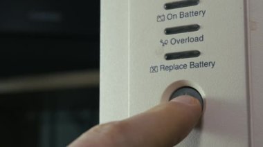 Beyaz bir kargo ünitesinin güç düğmesine basan bir parmağın yakın çekimi. Elektrik güvenliği, elektrik kesintisi koruması ve ev ofisi veya sunucu odasında veri güvencesi kavramı.