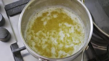 Gaz ocağındaki paslanmaz çelik tencerenin içinde erimiş yağ köpükleri ve köpükler. Ev yapımı yemek pişirme, tereyağı ve klasik süt ürünleri hazırlama kavramı.