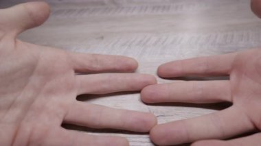 Bir adamın ellerinin birbirine doğru kaymasını ve parmaklarını hafif ahşap bir masanın üzerinde birleştirmesini. Bağlantı kavramı, ortaklık, düşünce ve insan dokunuşu..
