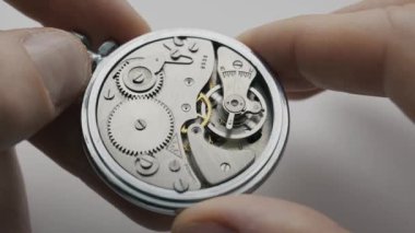 Eller, iç dişli mekanizmasını ve salınan denge çarkını gösteren açık gümüş bir cep saati tutuyor. Bu çekim hassas mühendisliği ve zamanın akışını ön plana çıkarıyor..