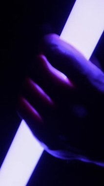 Bir elin silindirik bir LED ışık tüpünü tutarken yakın plan görüntüsü. Karanlıkta renkleri maviden mora ve sarıya çeviriyor. Konsept: partiler veya gelecekteki teknoloji için yaratıcı görsel efektler.