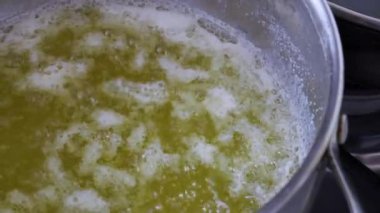 Metal bir tencerede kaynayan ve köpüren sarı sıvının yakın plan çekimi. Mutfak hazırlığı ve geleneksel yemek pişirme yöntemleri kavramı.