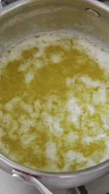 Altın sarısı eritilmiş tereyağı, yemek hazırlıkları sırasında gümüş bir tencerede güçlü bir şekilde kaynıyor. Mutfak malzemeleri kavramı, ghee yapmak, ev yemekleri, ve pişirme malzemeleri.