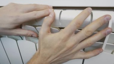 A man's hands touch a modern white bimetallic radiator, checking the temperature during the heating season. Concept of home comfort, warmth, and energy consumption.