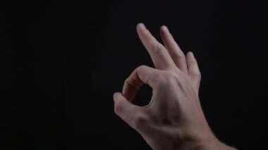 Bir adamın eli, stüdyo ortamında siyah bir zemine karşı A-OK sembolü yapar. Onay kavramı, mükemmellik, sözsüz iletişim, tatmin ve olumlu anlaşma.