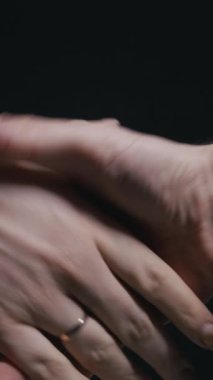 Karanlık bir arkaplanda sıkıca tokalaşan iki kişinin dikey yakın çekimi. İş ortaklığı kavramı, anlaşma, güven ve profesyonel anlaşma.