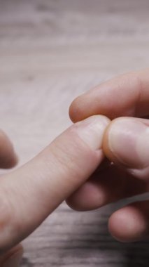 Tahta bir masanın üzerindeki tırnak ve beyaz noktaları yakından inceleyen kişi. Bu dikey video tırnak sağlığı sorunları, kuru cilt ya da kişisel bakım konularını vurgular.