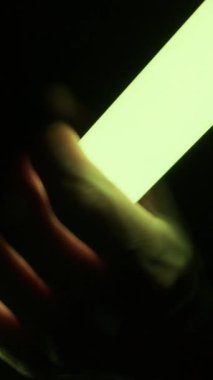 Yakından bakıldığında, karanlıkta canlı renklerde kayan parıldayan bir LED tüpü tutan bir el görülüyor. Yaratıcı ışıklandırma teknolojisi, gece hayatı ve gelecekteki estetik kavramı.