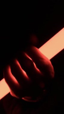 Pürüzsüz bir zemin üzerine kırmızı bir LED ışık tüpünü sıkıca tutan bir elin yakın plan görüntüsü. Kaygı verici güç kavramı, gelecekteki savaş ve gizemli bilim kurgu teması.