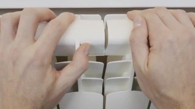 Male hands touch and hold the fins of a white central heating radiator to check the temperature. Concept of heating efficiency, cold winter weather, and rising energy utility bills.